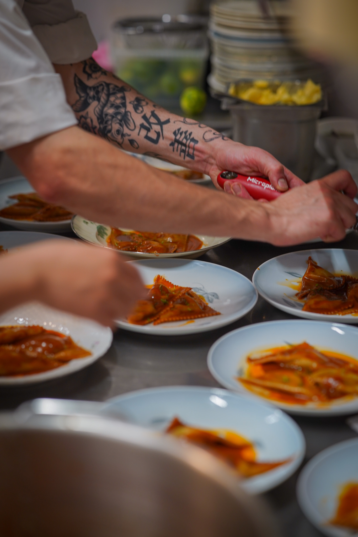 Tattooed forearm grating over plated pasta dishes