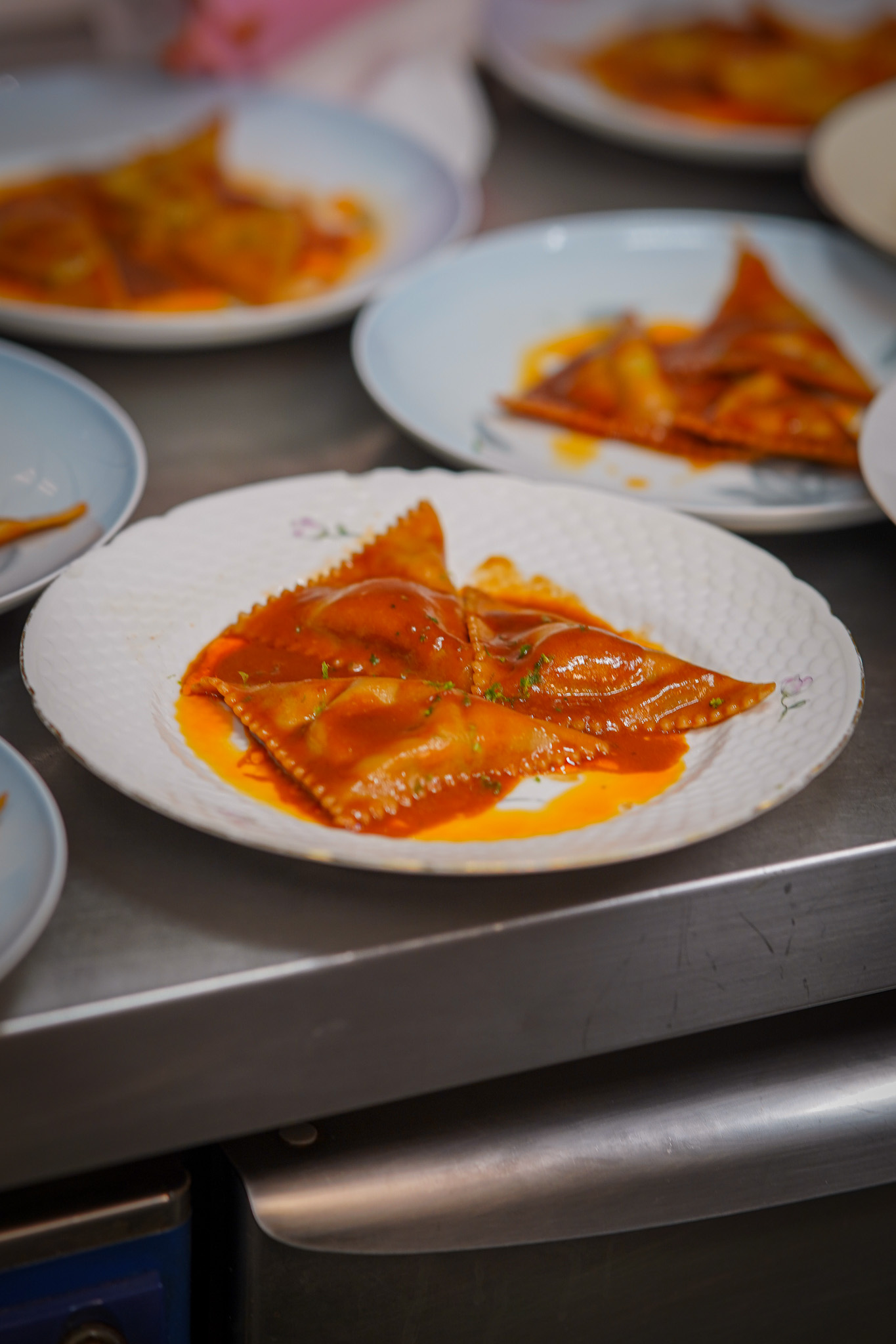 Plated pasta triangles in red sauce, several plates in a row